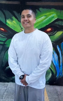 Ediberto smiles in front of a vibrant green and blue graffiti mural.