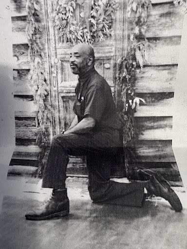 Jeffery kneels in front of a wooden door decorated with hanging greenery.