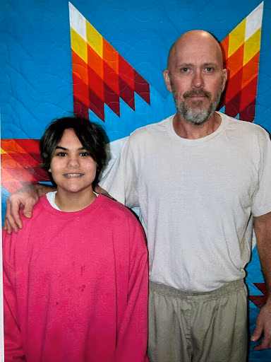 Mike and Stacy, 63, posing together in front of a colorful quilt.