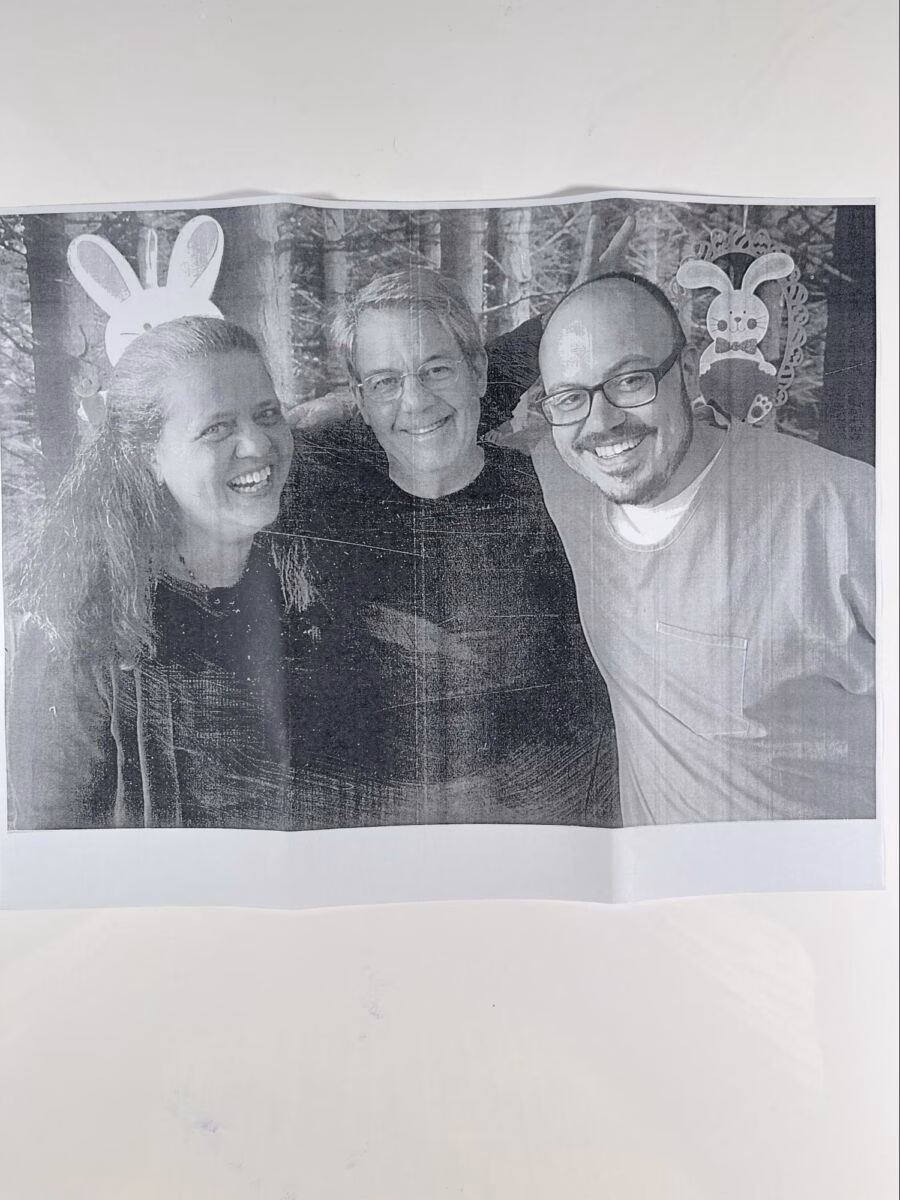 Three smiling people posing together in a forest, with a woman wearing a white bunny headband and a decorative bunny sign in the background.