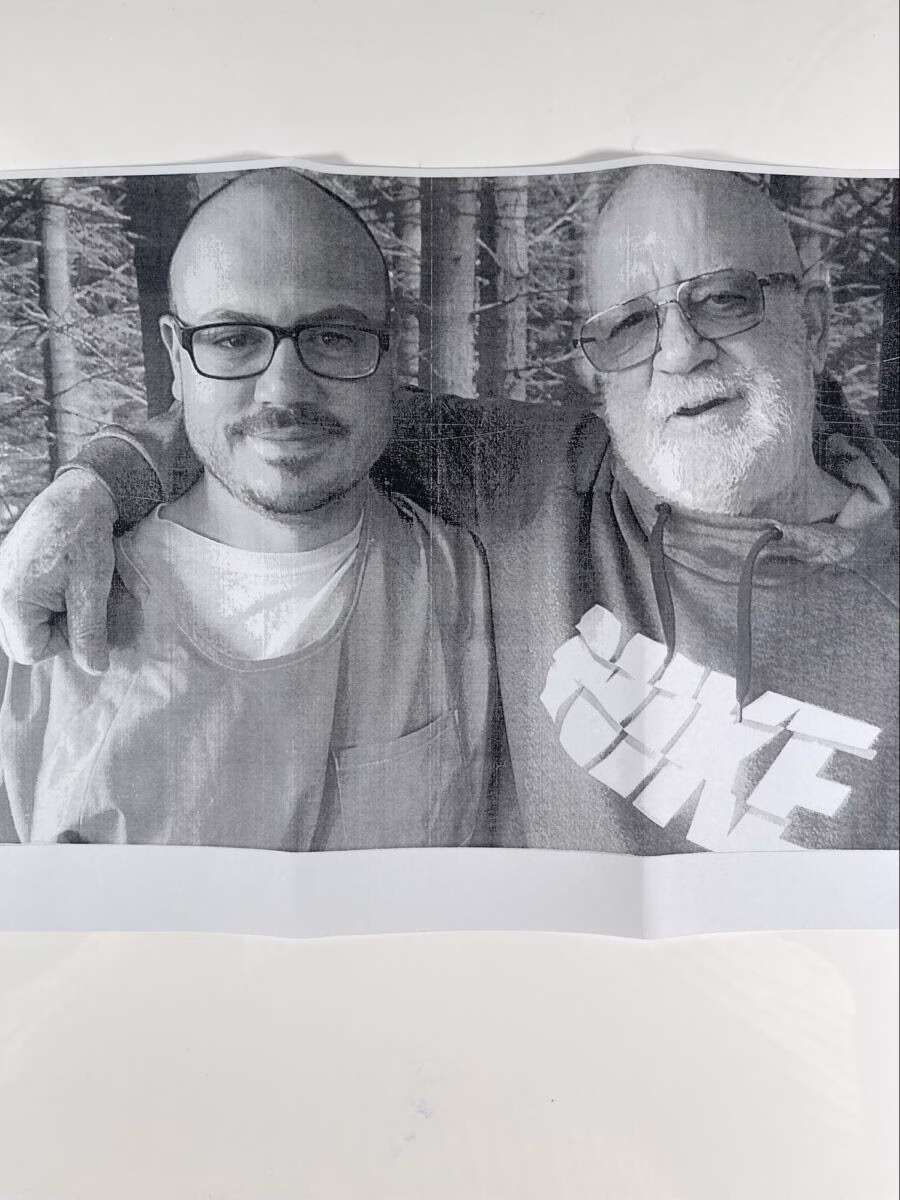 A black and white photograph of two men, Alexander and an older man, posing together in a forest.