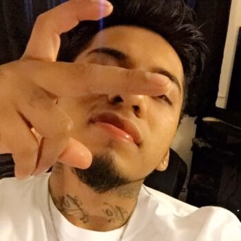 Selfie of Marcos, 28, with a hand gesture over his face, showing neck tattoos.