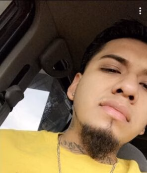 Selfie of Marcos, 28, with a goatee and neck tattoos, wearing a yellow shirt inside a car.
