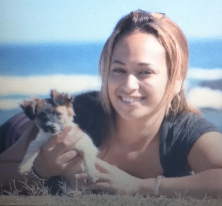 IMG_1378 Justina, 30, smiling while holding a small dog on a beach.