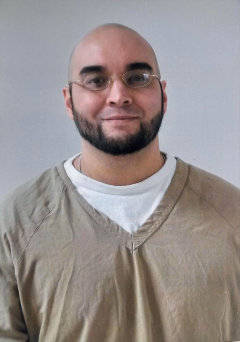 Portrait of Eric, 49, a bald man with a beard and glasses, wearing a tan shirt over a white t-shirt.