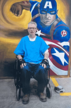 Brian, 55, sits in a wheelchair in front of a large mural of Captain America.