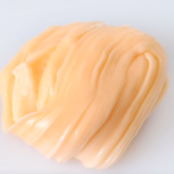 A single piece of homemade salt water taffy with a smooth, glossy, pale orange surface and soft folds against a white background.
