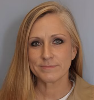 Portrait of Sabrina, 51, a woman with long blonde hair and green eyes, wearing a tan jacket over a white shirt.