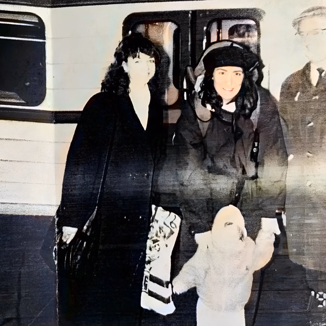 A vintage photograph of three people, including a child in a white hooded coat, standing in front of a train.