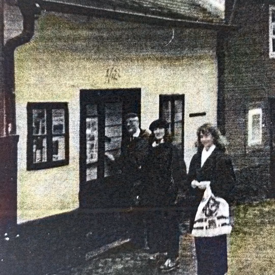 Three people stand in front of a building with a sign that reads '442'.