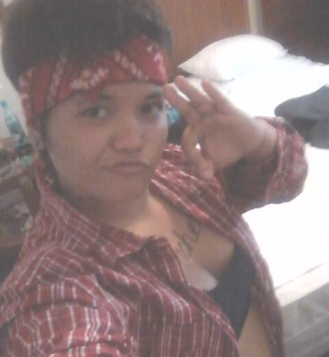 Melanie, 34, wearing a red patterned headband and plaid shirt, makes an 'OK' sign with her hand.