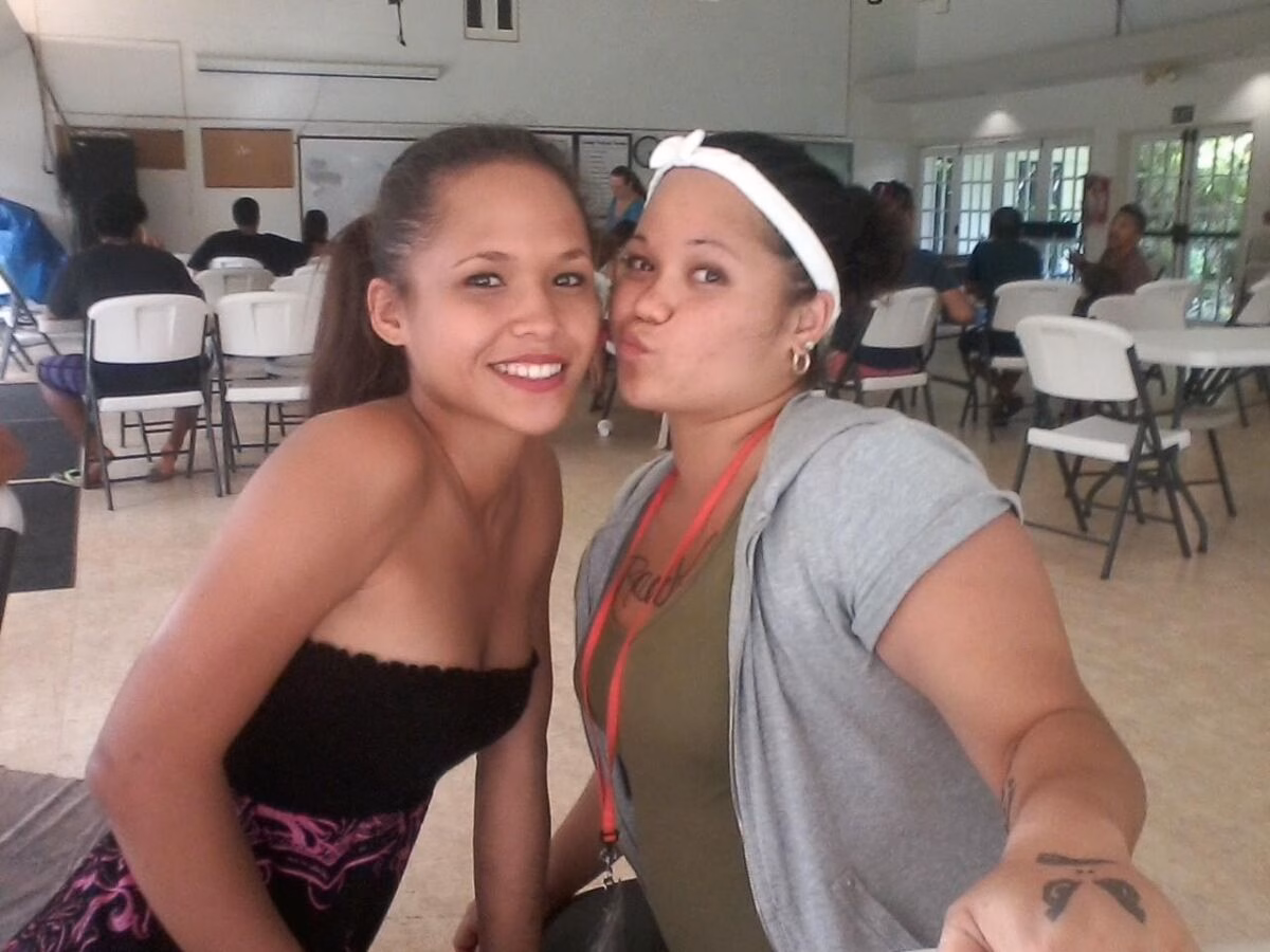 Two women posing for a selfie in a large room with white chairs and tables in the background.