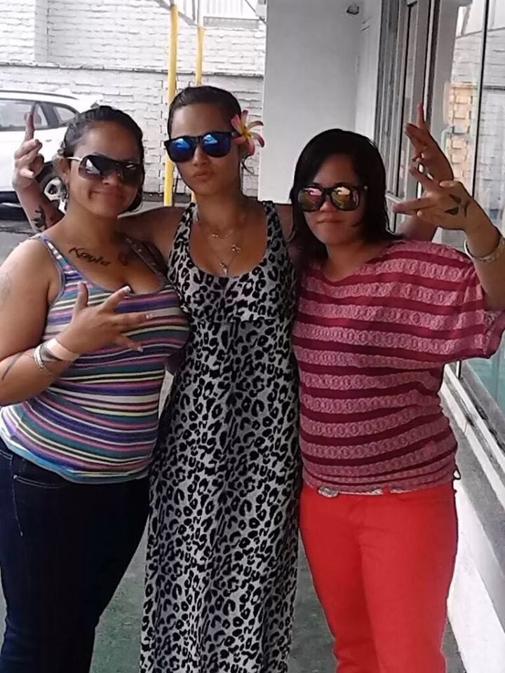 Three women posing together outdoors, each making a peace sign with their hands.