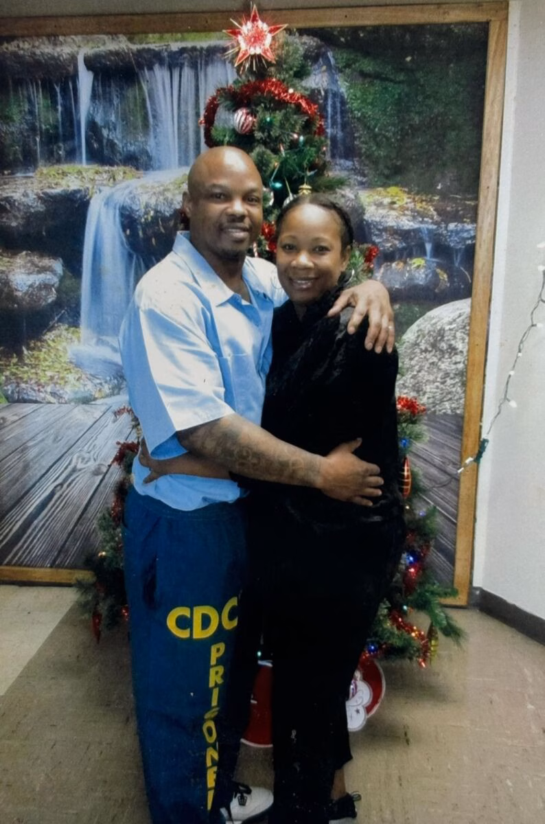 Duane, 57, and a woman embrace in front of a Christmas tree and a waterfall mural.