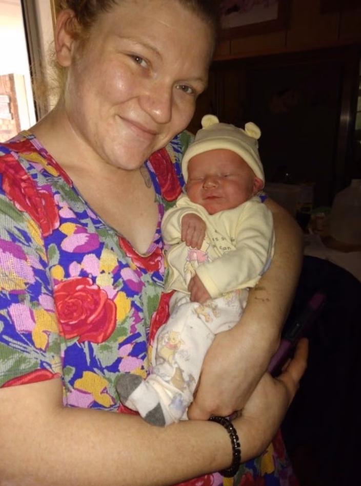 Miranda holds a newborn baby wearing a yellow hat with bear ears.
