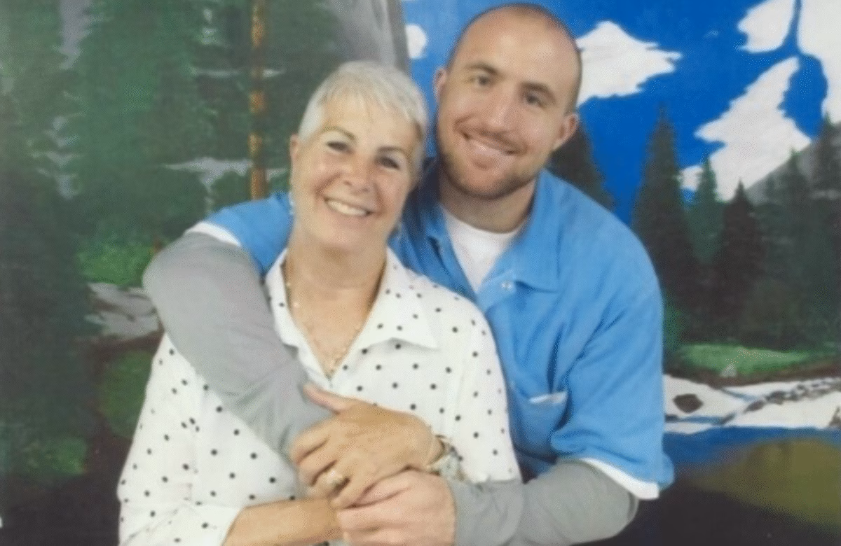Anthony, 38, smiles with an older woman in front of a painted forest backdrop.
