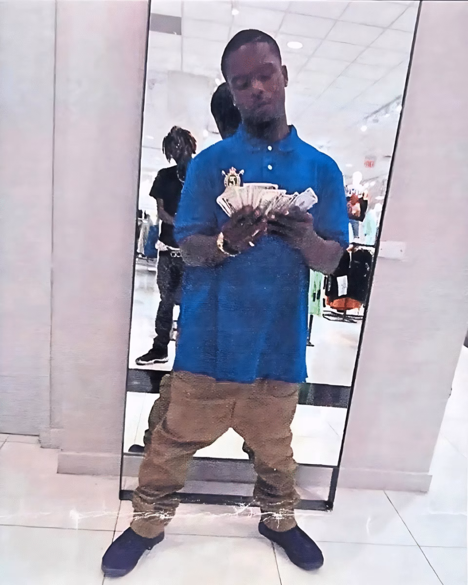 image14 A man in a blue polo shirt and brown pants stands in a mirror, fanning a large stack of cash. Another person is visible in the reflection behind him.