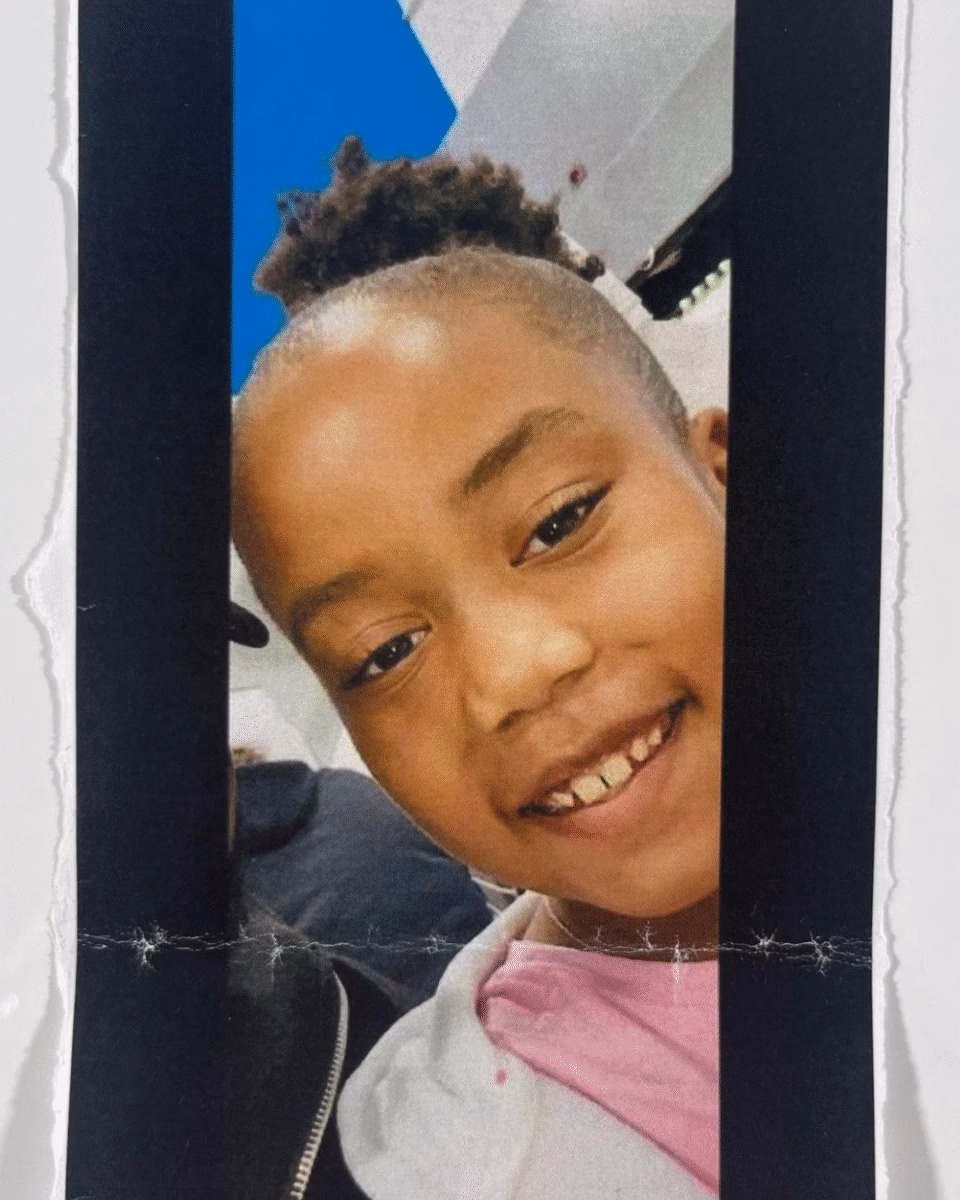 image18 A close-up portrait of a young person with a shaved head and a small topknot, smiling at the camera.