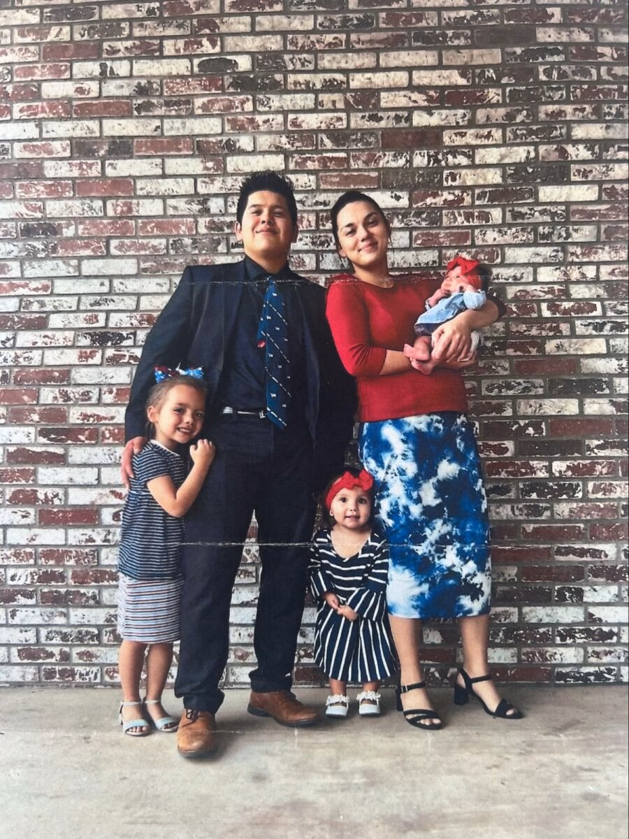 A family of five, including David, stands together in front of a weathered brick wall.