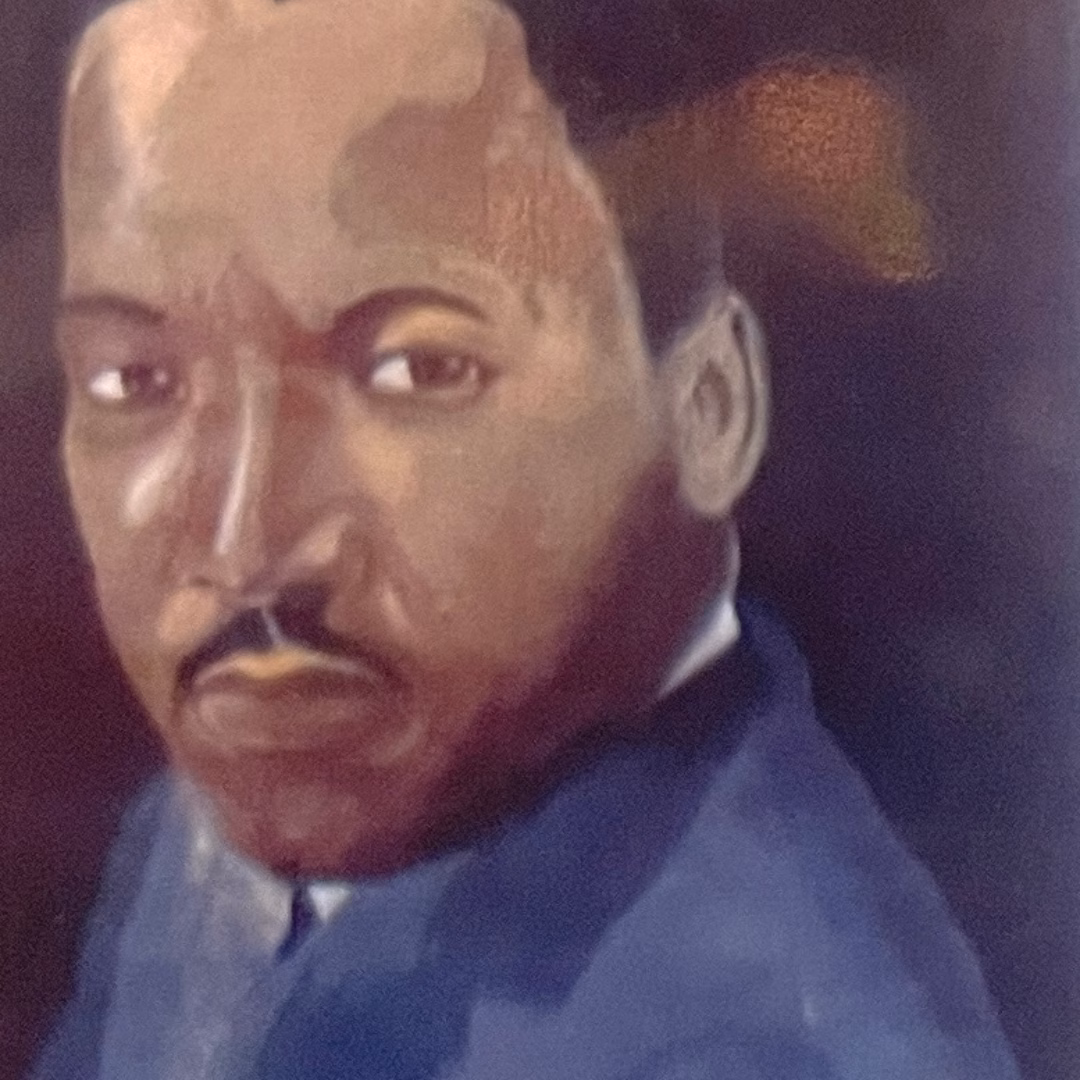 Portrait of Martin Luther King Jr. in a blue suit, shown from the chest up against a dark background.