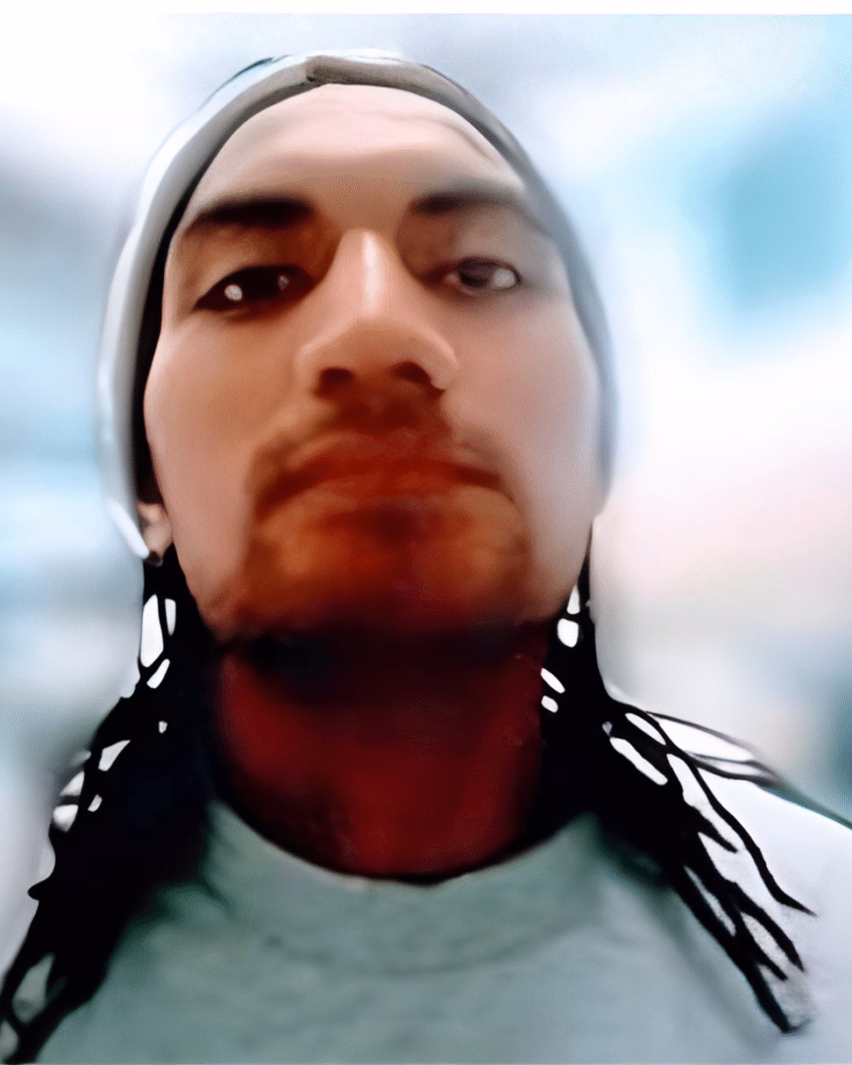 Close-up portrait of Thomas, 31, wearing a grey beanie and a light-colored shirt with black and white patterned details on the shoulders.