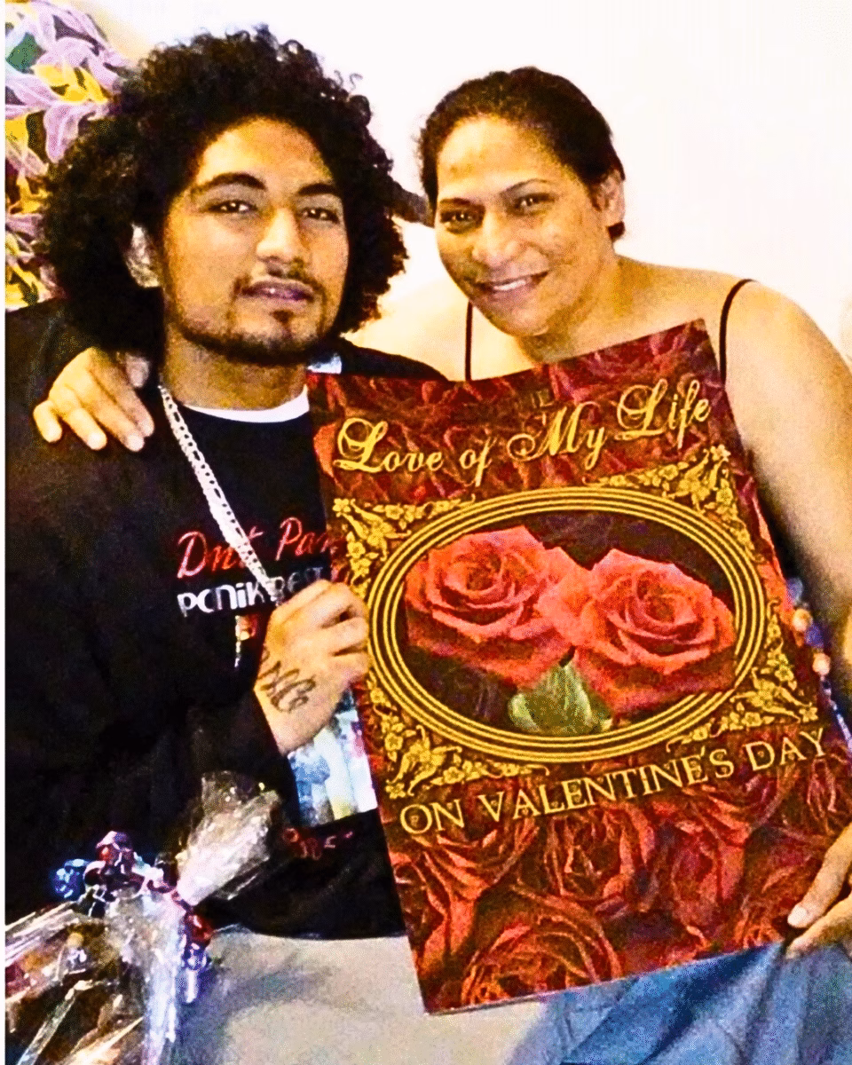 A man and a woman pose together, holding a Valentine's Day card that reads 'The Love of My Life' and 'On Valentine's Day', featuring a central image of two red roses.