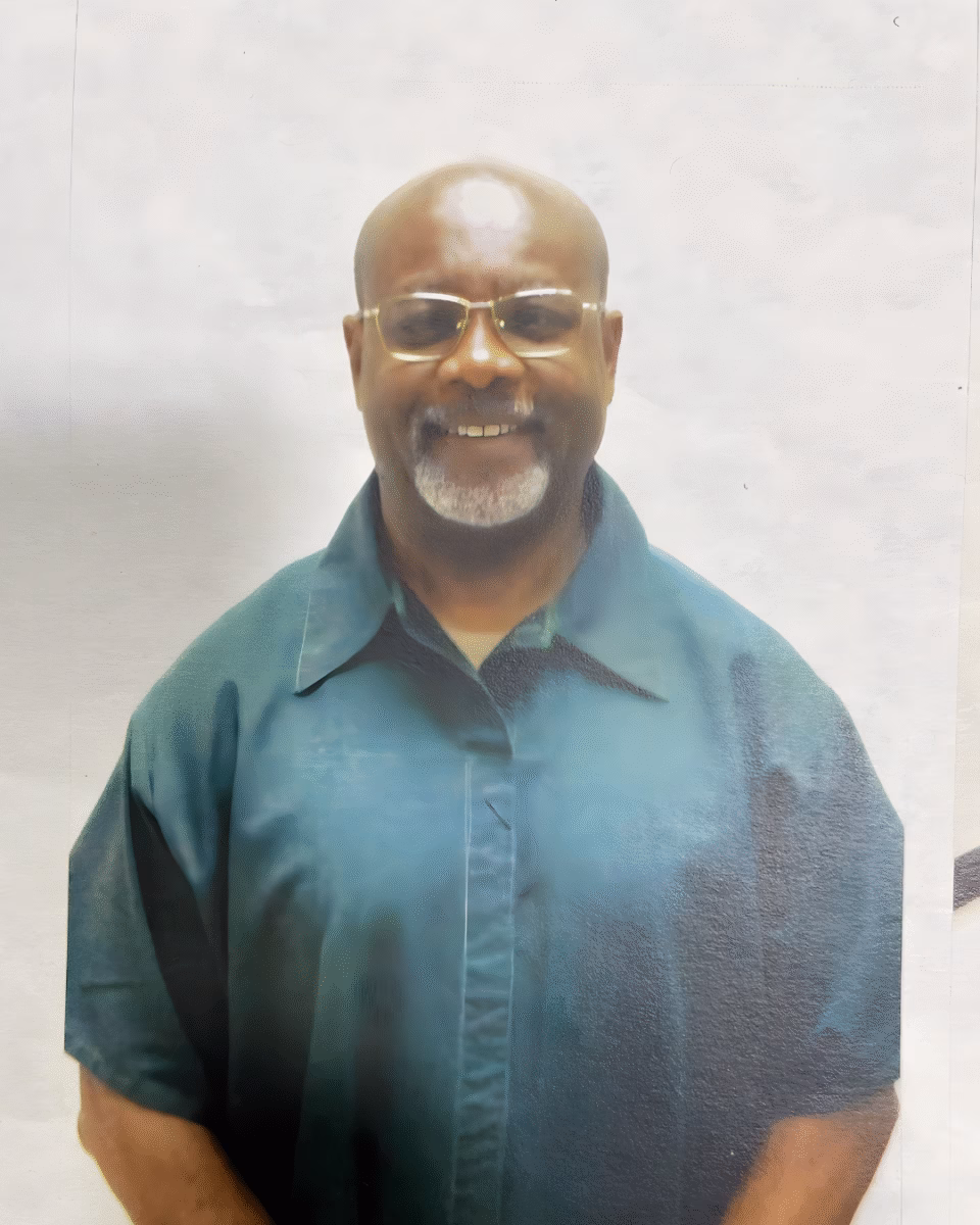 8 Portrait of Charles, a bald man with a white goatee and glasses, wearing a teal button-down shirt.