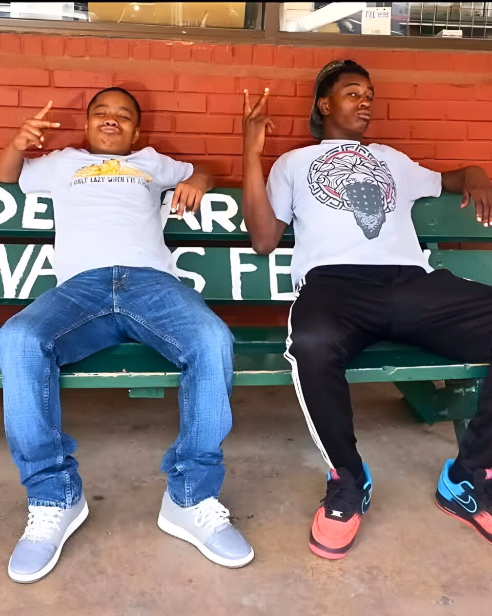 Diyondré Wilson and a friend sit on a green bench against a red brick wall, both making peace signs.