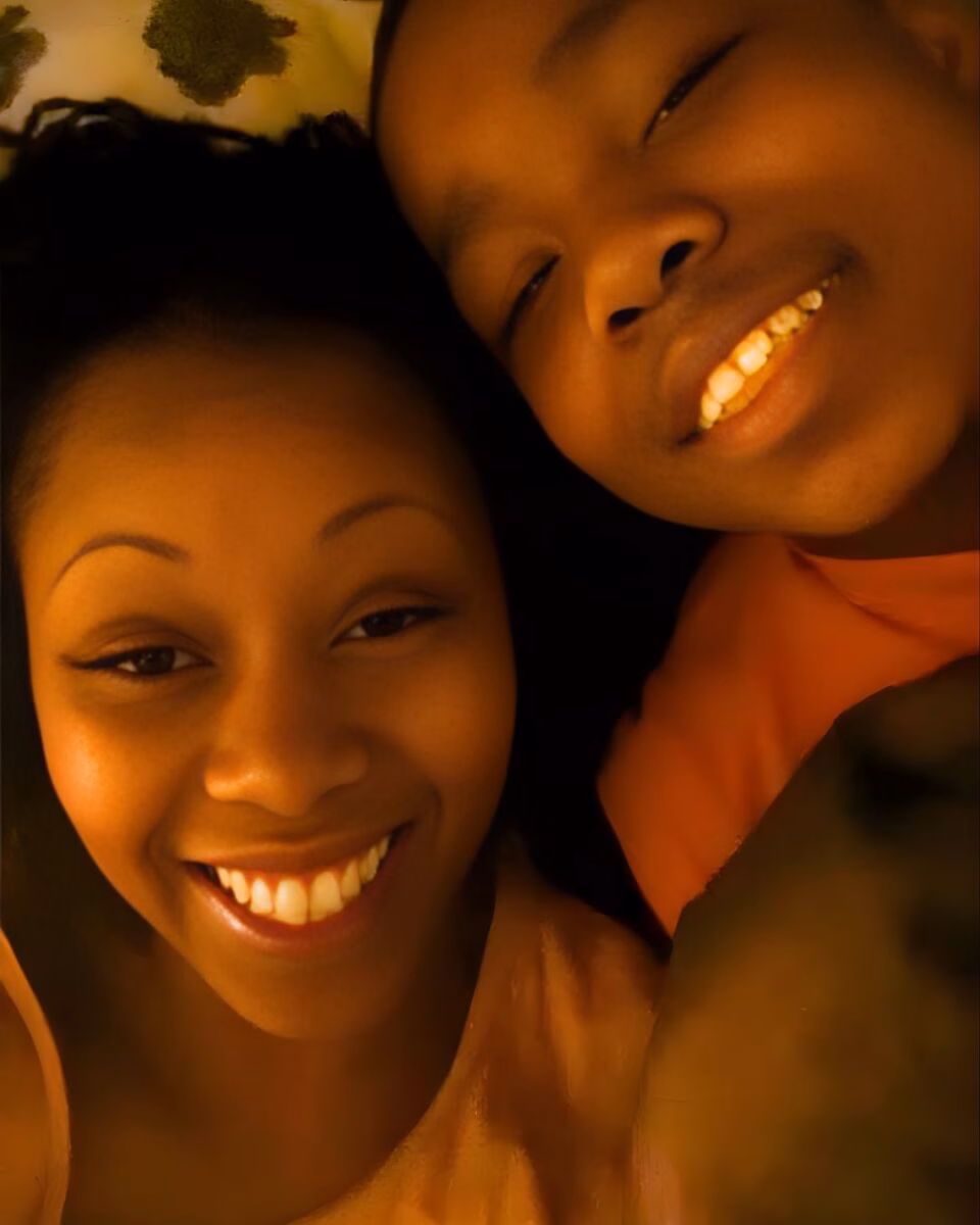 A close-up selfie of Diyondré Wilson and a young boy smiling together under warm, orange-toned lighting.
