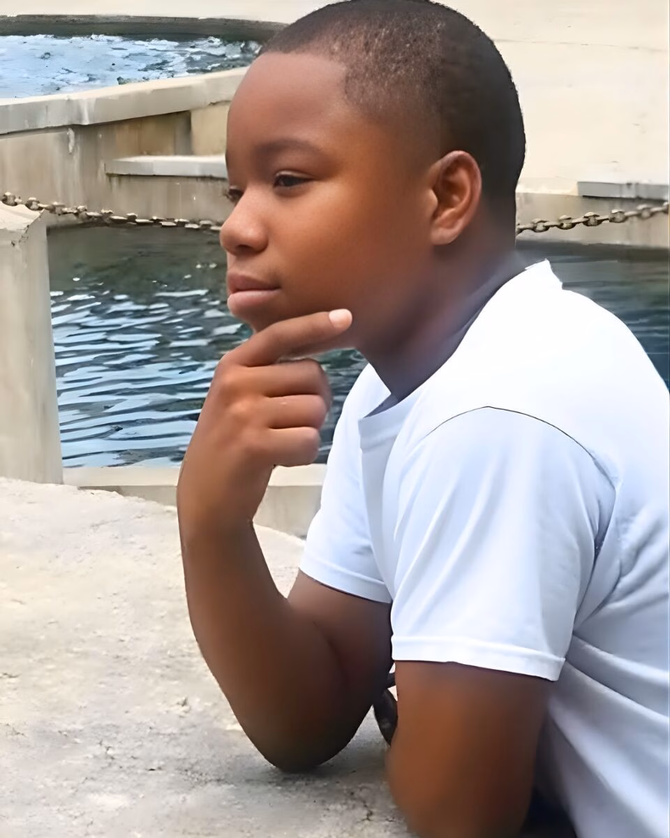 Diyondré Wilson, a young boy in a white t-shirt, rests his chin on his hand in a contemplative pose by a concrete pool.