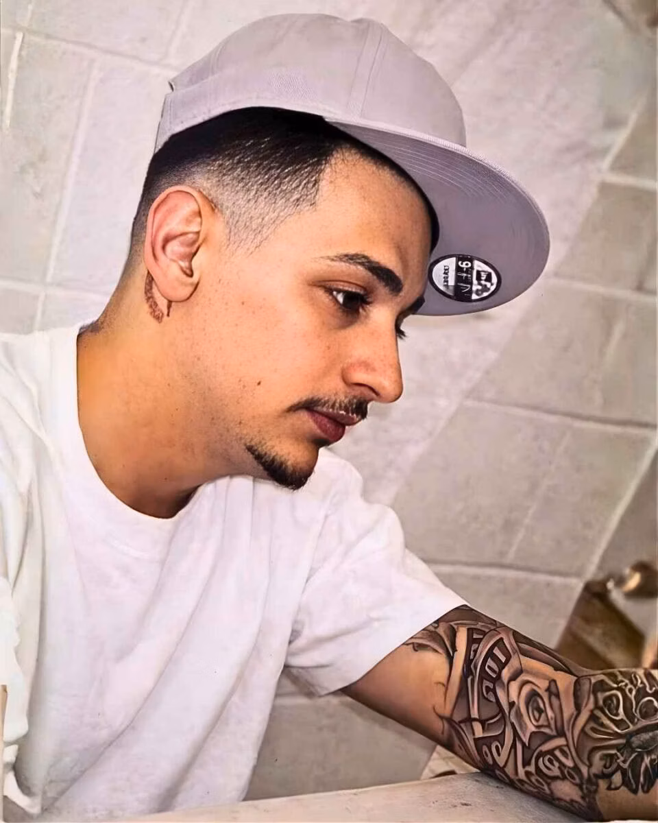 Robert Ortiz (1) Robert Ortiz, 32, wearing a grey New Era cap and white t-shirt, with a detailed tattoo on his left forearm and a small tattoo on his neck.