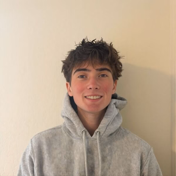 AlexKing smiling in a grey hoodie against a plain wall.
