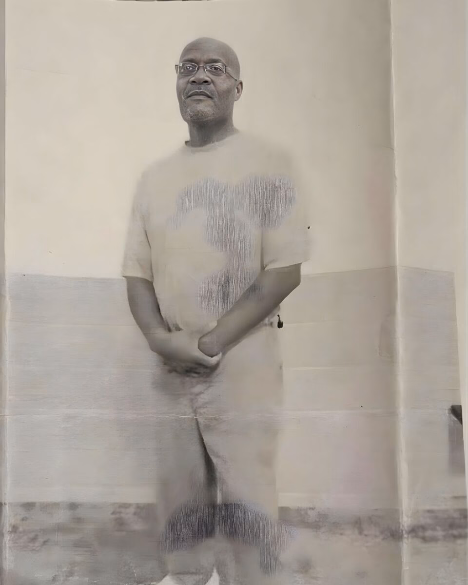 Lionel Lewis Rogers, a bald man with glasses and a goatee, stands in a light-colored room with his hands clasped in front of him.