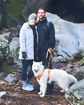 Justin Cooksey and a woman stand with a white Samoyed dog on a rocky trail.