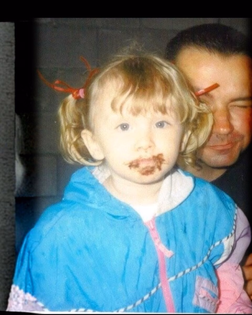 Julia Marcinak (1) A young girl with chocolate on her face, wearing a blue jacket, with a man in the background.