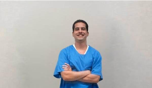 RandyT in blue scrubs with arms crossed, smiling against a plain wall.