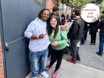 A man and a woman posing together at an outdoor gathering, with a man in a white hoodie and a woman in a green sweatshirt.