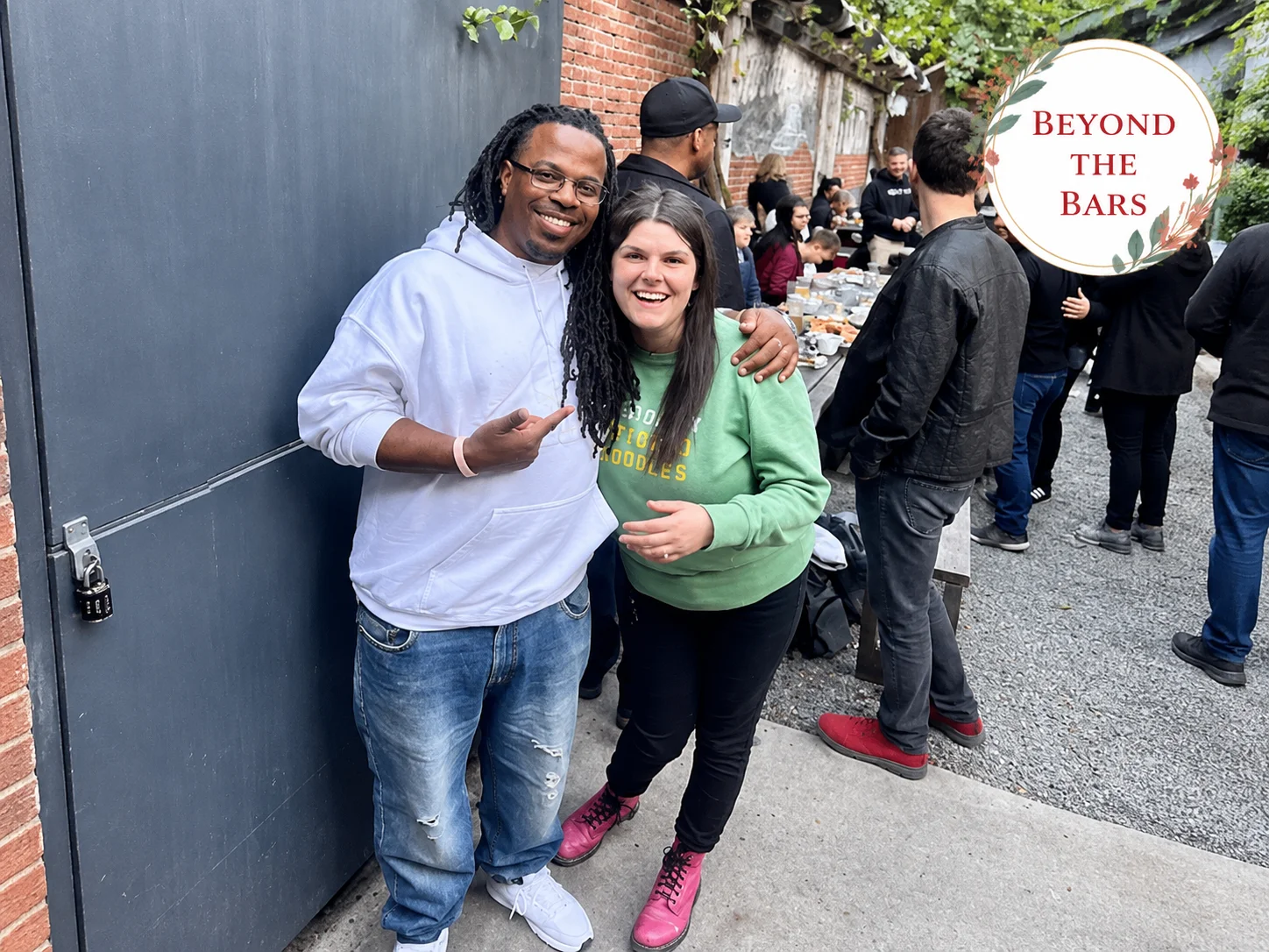 Philippe "Kells" Kelly, 16 years inside 10 A man and a woman posing together at an outdoor gathering, with a man in a white hoodie and a woman in a green sweatshirt.