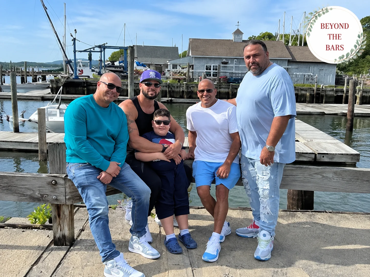 Five people, including a child, pose together on a wooden dock in front of a harbor with boats and buildings.
