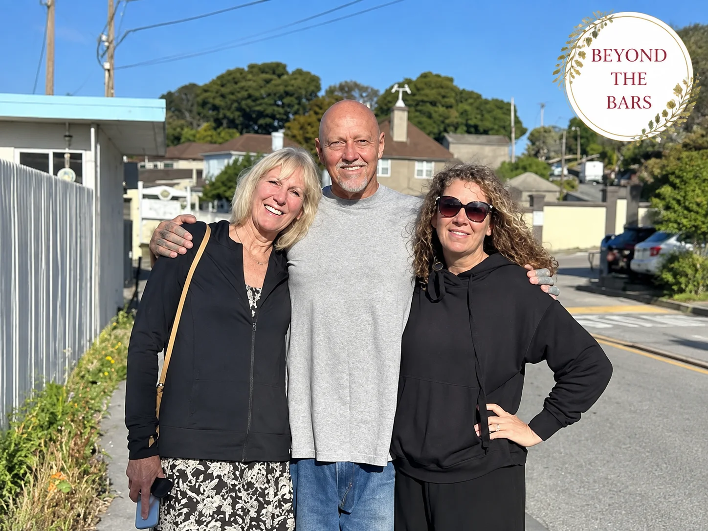 Three people, Bruce and two women, standing together on a sidewalk in a residential neighborhood.